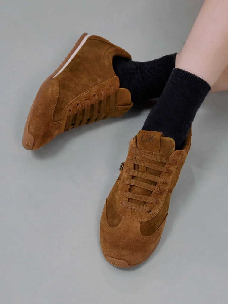 Brązowe zamszowe sneakersy o niskim profilu i smukłej sylwetce.